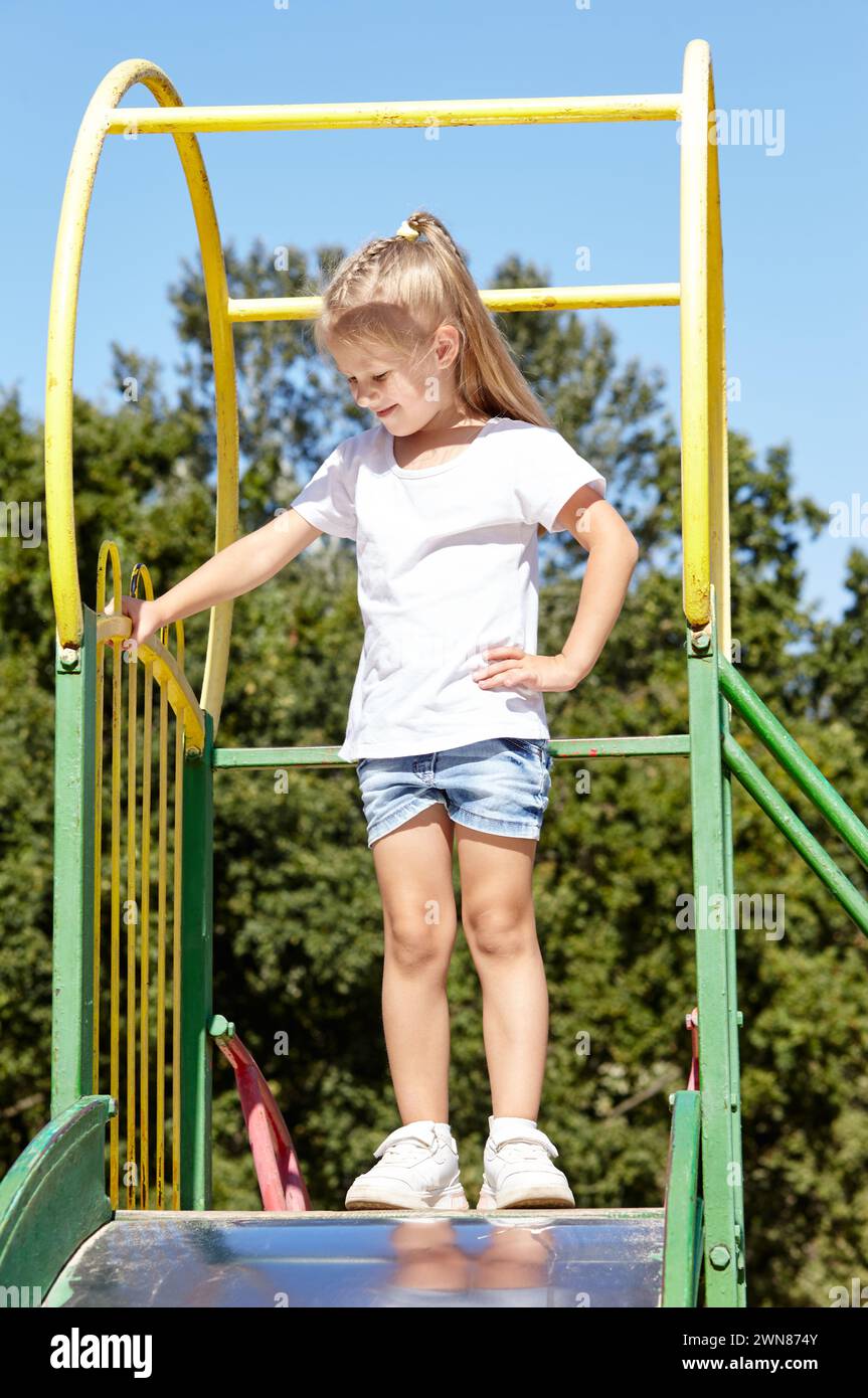 Kleines Mädchen, das auf einer Rutsche auf einem Spielplatz im Sommer-Stadtpark spielt. Kindheit, Freizeit und Menschenkonzept - glückliche Kinderruhe und viel Spaß Stockfoto