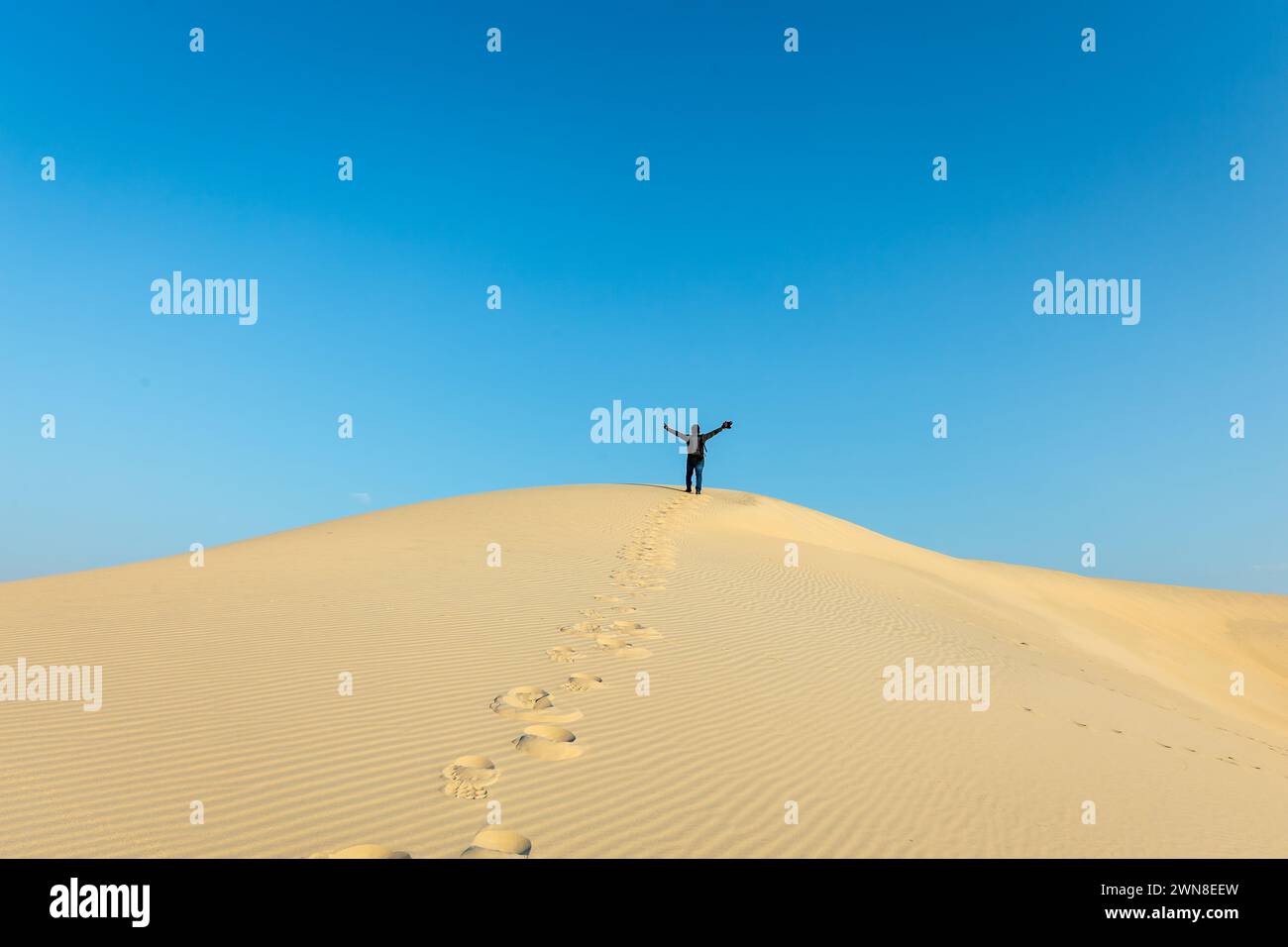 Ein männlicher Fotograf, der Schritt für Schritt durch die Wüstenlandschaft in Abqaiq Dammam Saudi Arabien spaziert. Stockfoto