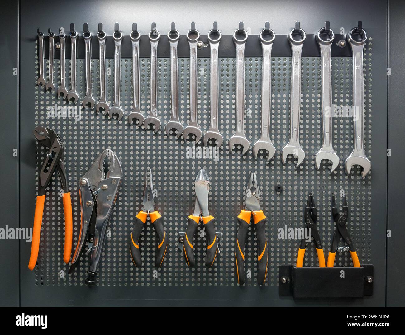 Satz von Schraubenschlüsseln und Zangen, die üblicherweise von Mechanikern für die Wartung von Motoren verwendet werden, die in der Werkstatt an der Werkzeugtafel hängen Stockfoto