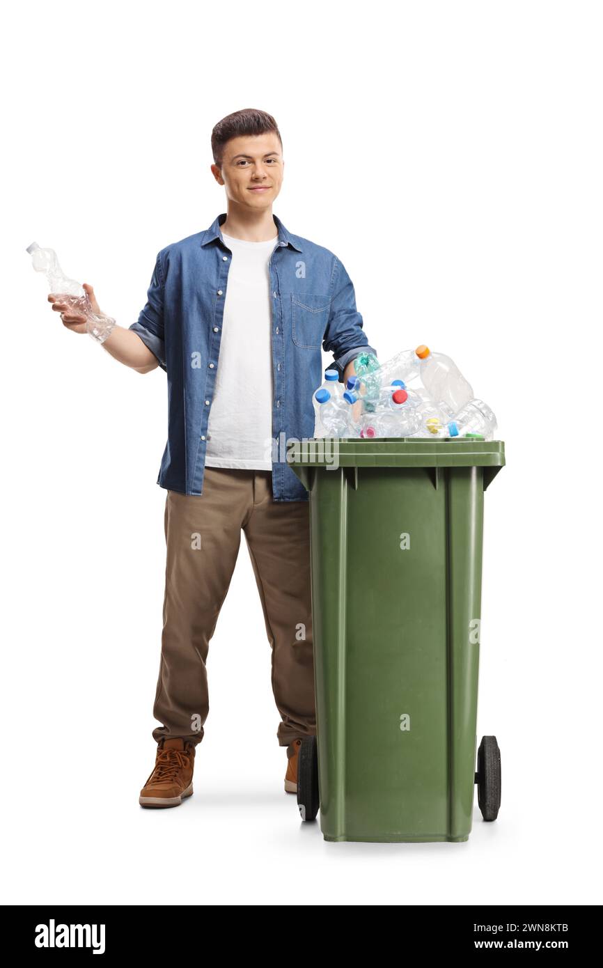 Junger Mann hinter einem Mülleimer, der eine Plastikflasche zum Recycling hält, isoliert auf weißem Hintergrund Stockfoto