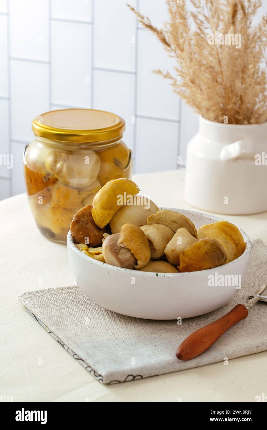 Eingelegte Pilze in einem Glas und auf einem Teller auf dem Tisch Stockfoto