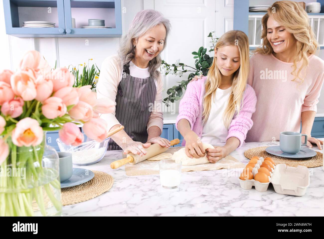 Drei Generationen von Frauen versammeln sich in der gemütlichen Küche, machen und Rollen Teig zusammen mit Lächeln und Lachen aus. Großmutter unterrichtet ihre Tochter und g Stockfoto