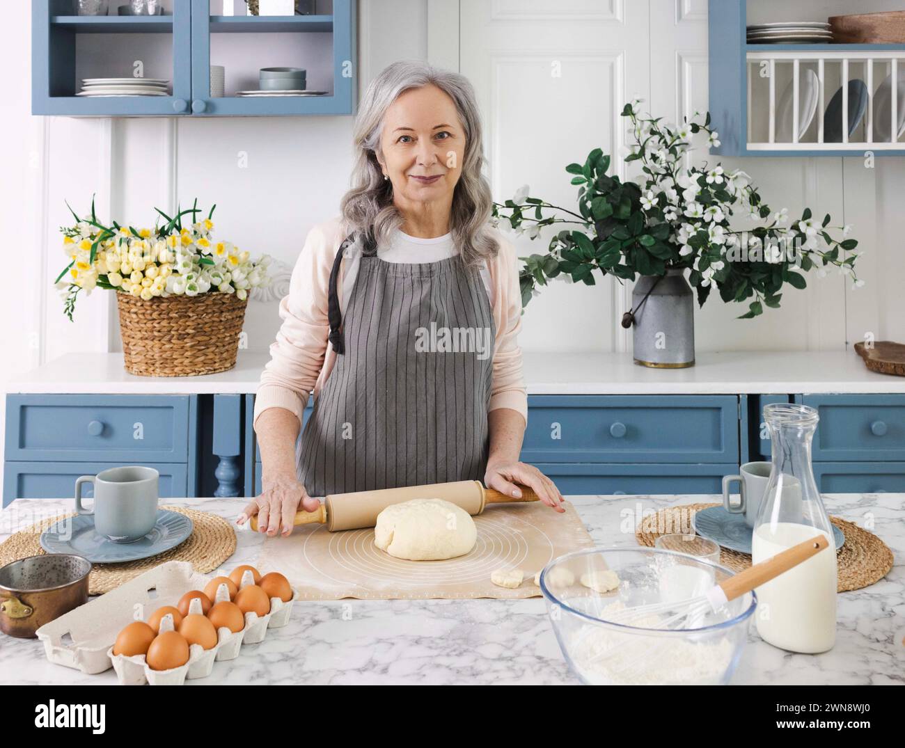 Silberhaarige Großmutter rollt anmutig Teig mit einer Nudelnadel für duftende Großmutters Gebäck und Croissants. Ältere Frauengeneration Stockfoto