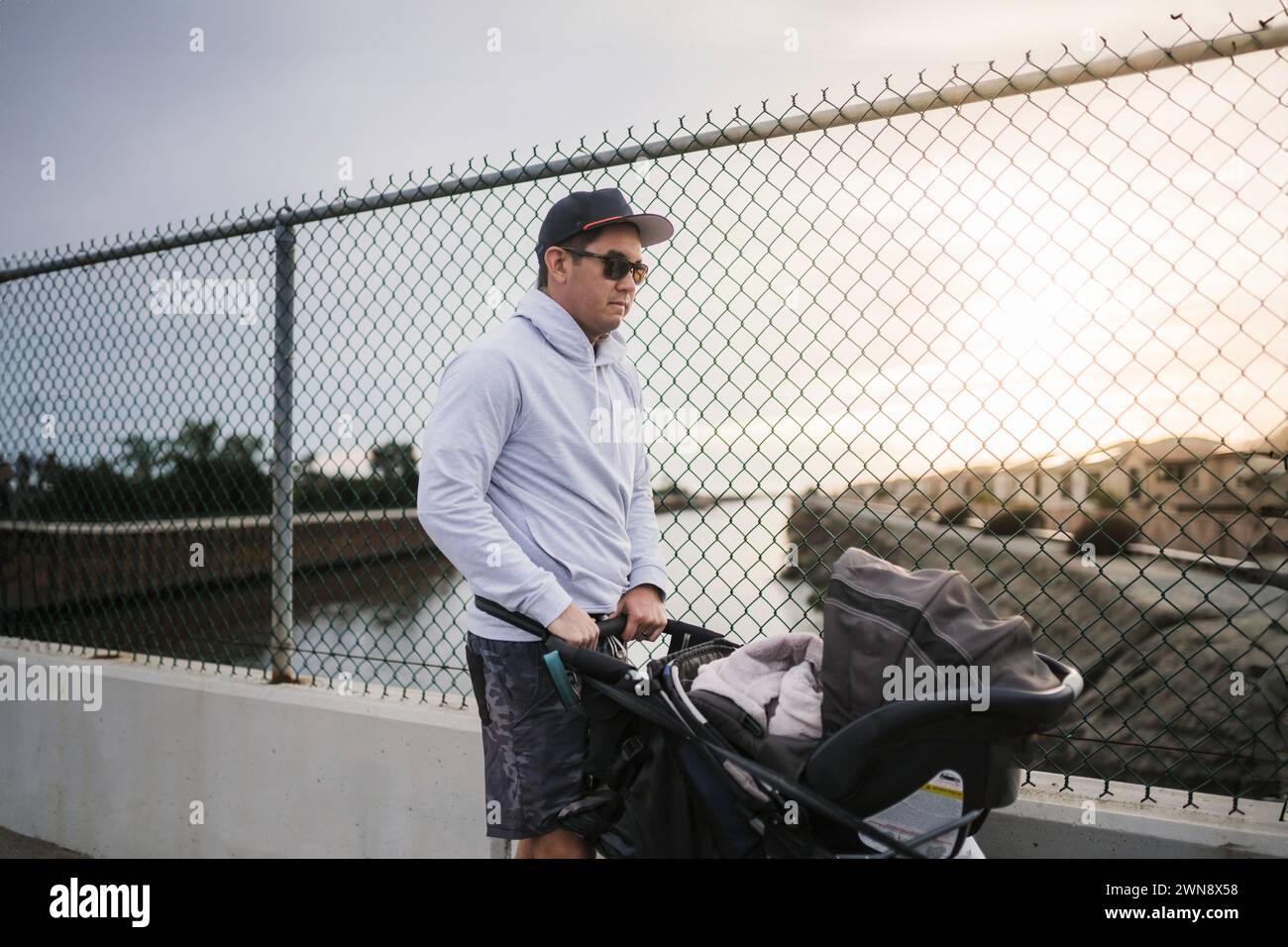 Mann mit Hut und Sonnenbrille, der das Baby in den Kinderwagen auf der Brücke schiebt Stockfoto