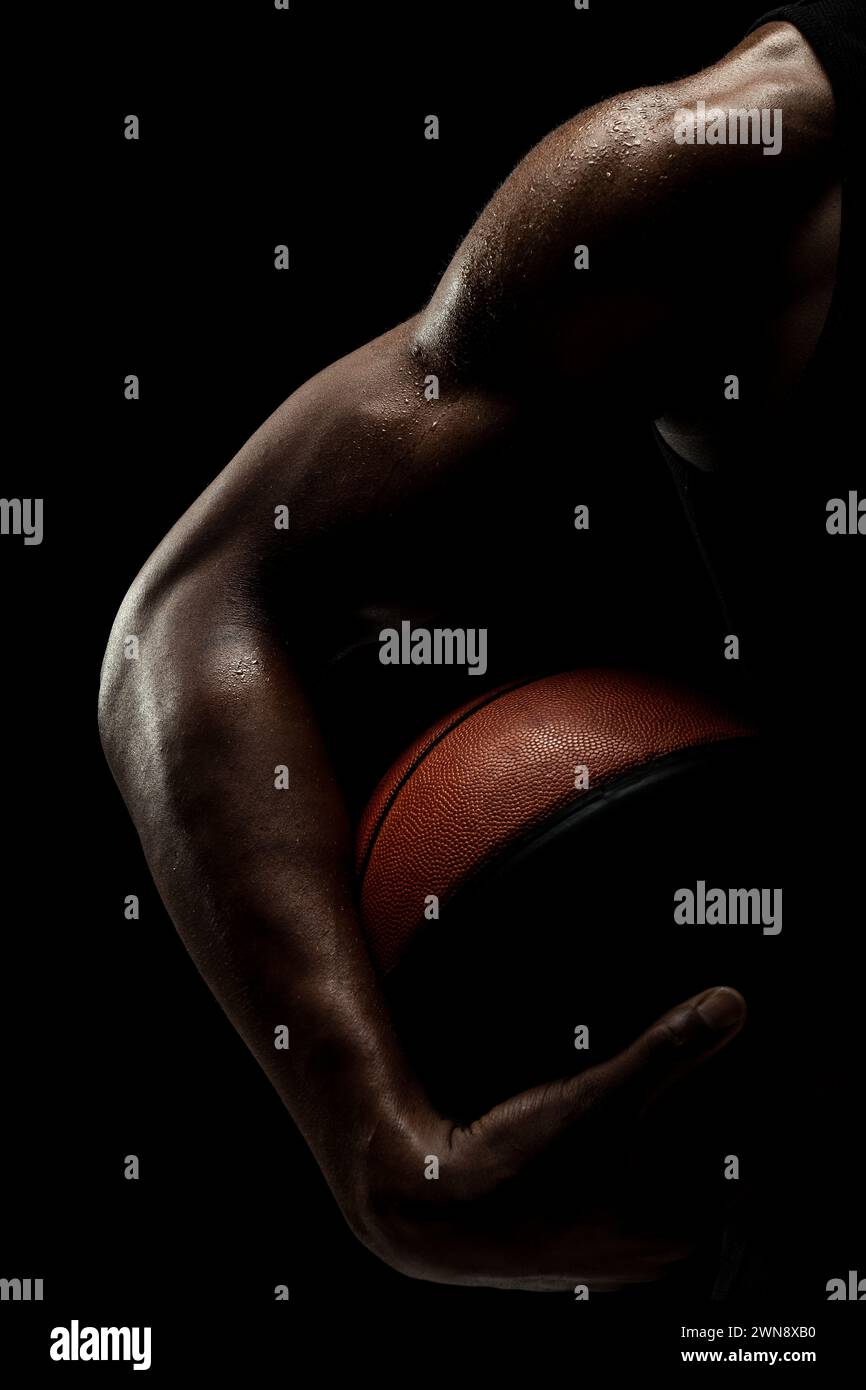 Basketballspieler hält einen Ball vor schwarzem Hintergrund. Abstrakter männlicher Körper des afroamerikanischen Mannes. Muskulöse Person Seitensilhouette. Stockfoto