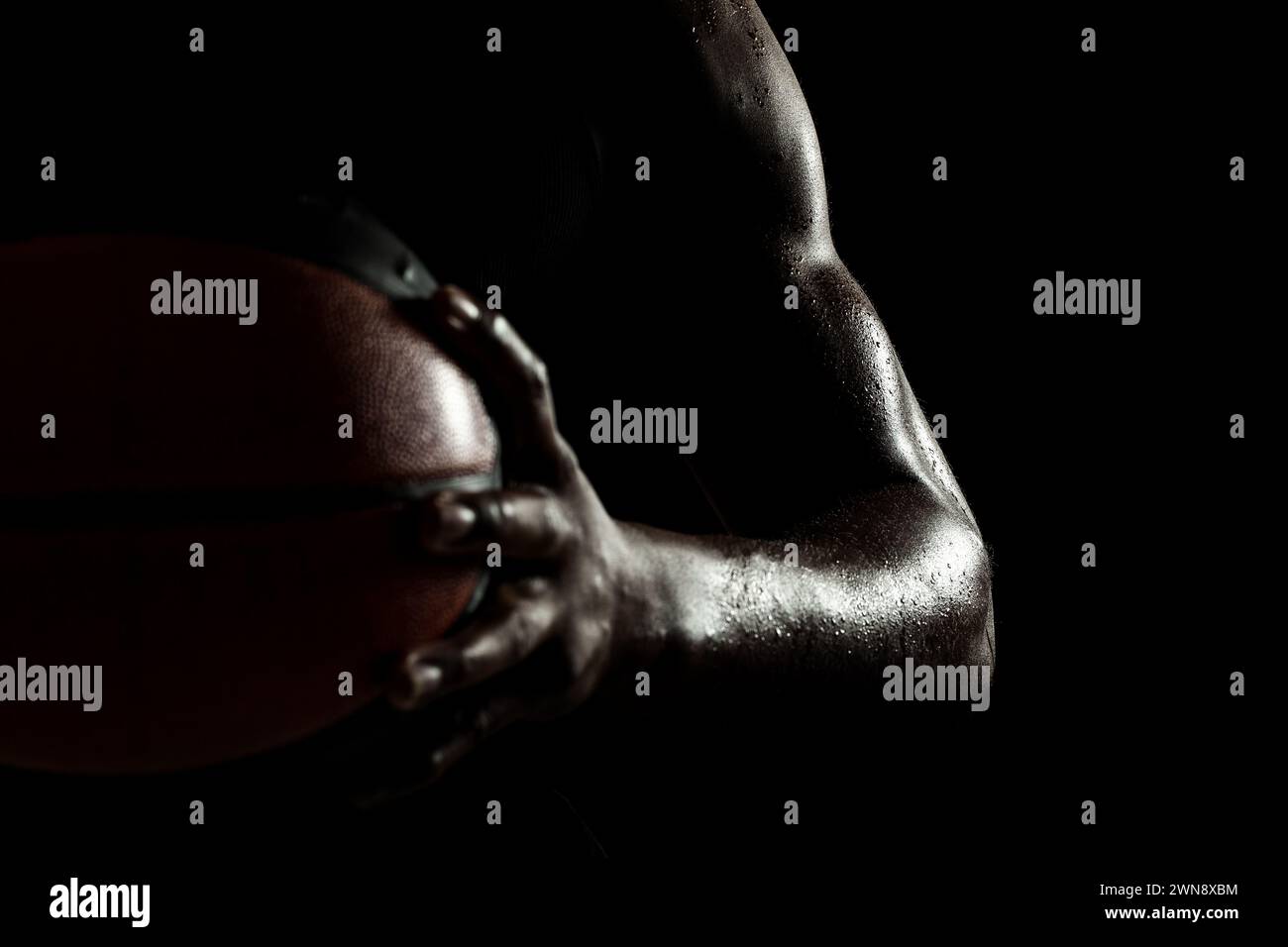 Basketballspieler hält einen Ball vor schwarzem Hintergrund. Abstrakter nasser männlicher Körper eines afroamerikanischen Mannes. Muskulöse Person Seitensilhouette. Stockfoto