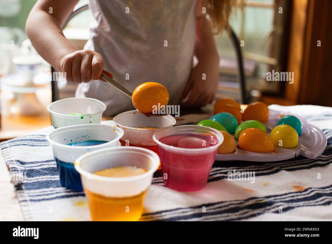 Ein Kind hebt ein orangenes Osterei aus der Lebensmittelfarbe Stockfoto