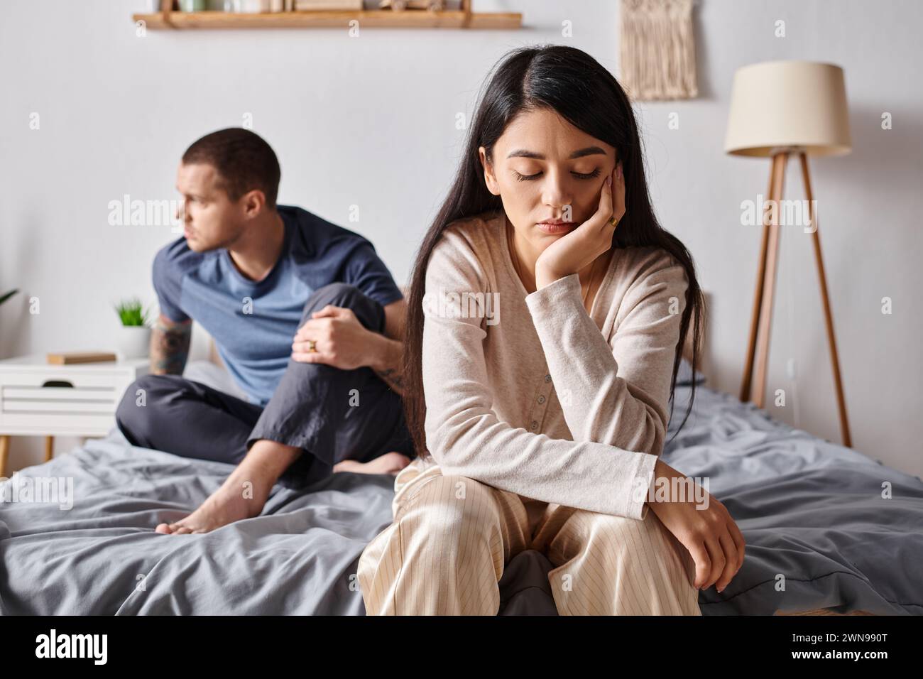 Junge und frustrierte interrassische Paare, die zu Hause im Schlafzimmer sitzen, Beziehungsschwierigkeiten Stockfoto