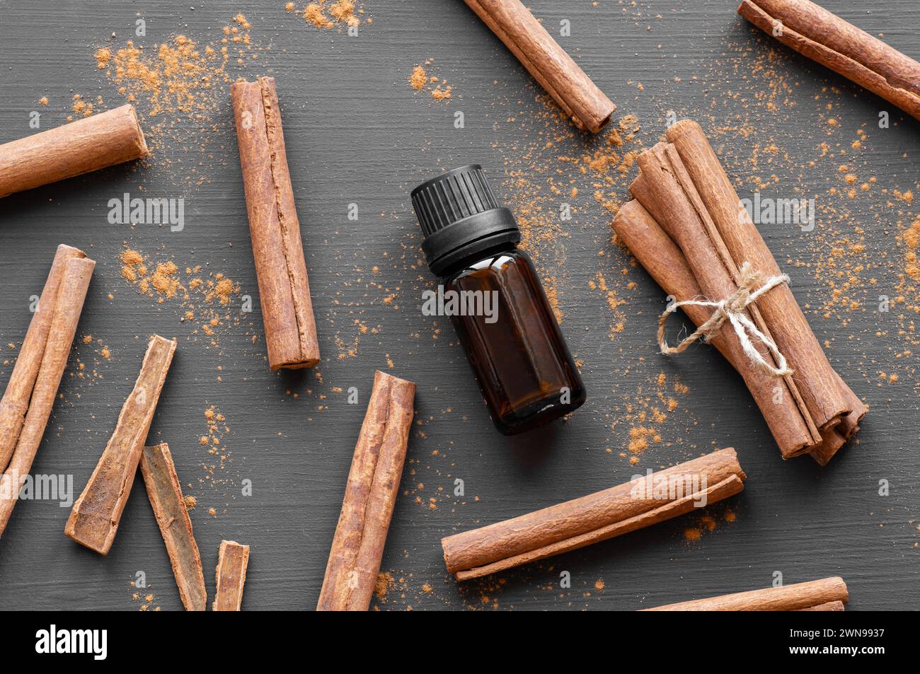 Glasflasche mit ätherischem Zimtöl mit Zimtstäbchen und Pulver auf dunklem rustikalem Hintergrund, alternative Medizin Stockfoto