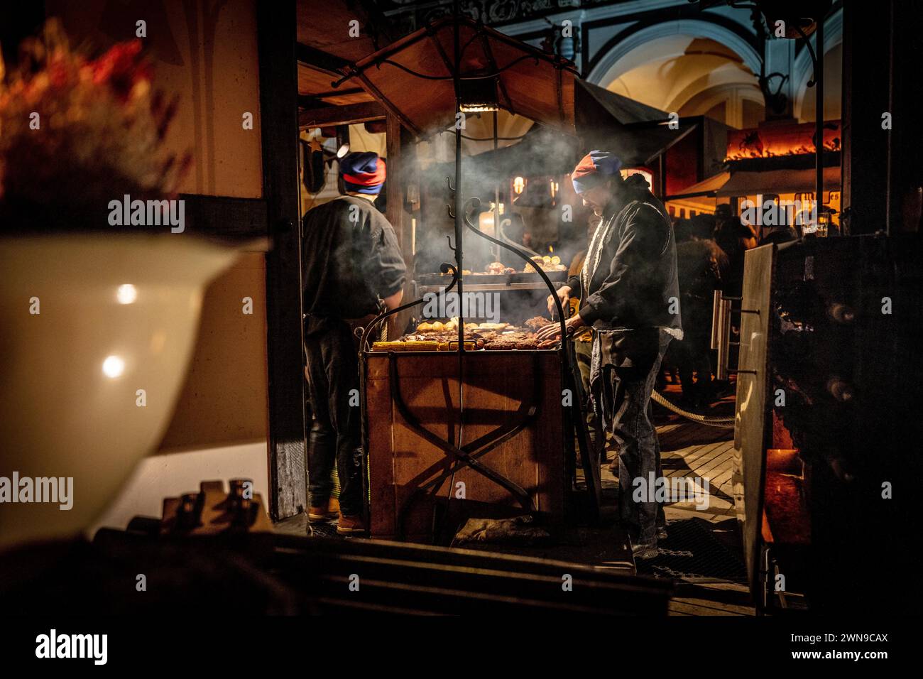 Arbeiter, die nachts an einem Marktstand grillen, umgeben von warmem Licht und Rauch, Weihnachtsmarkt Dresden Stockfoto