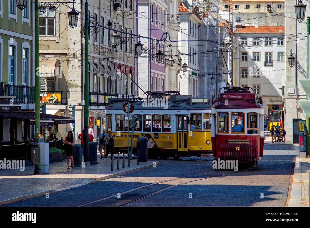 Historische Straßenbahnen fahren durch eine belebte Straße im sonnigen Lissabon, umgeben von klassischer Architektur, Lissabon Stockfoto