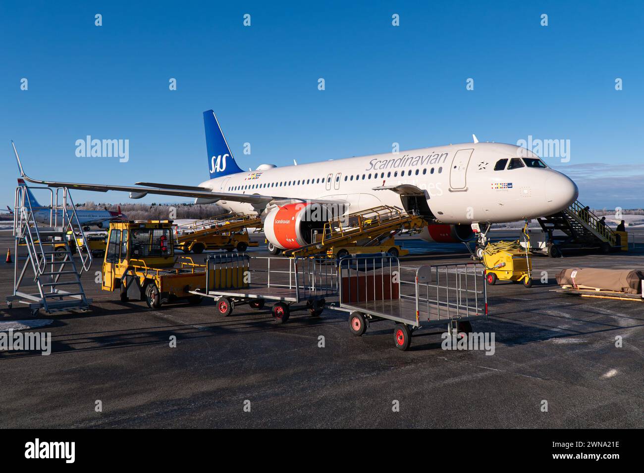 Ein SAS-Flugzeug (scandinavian Airline Systems), Airbus A320 NEO, am Flughafen Umeå, mit laufenden Bodenabfertigungsdiensten. Winterliche Bedingungen, blauer Himmel Stockfoto