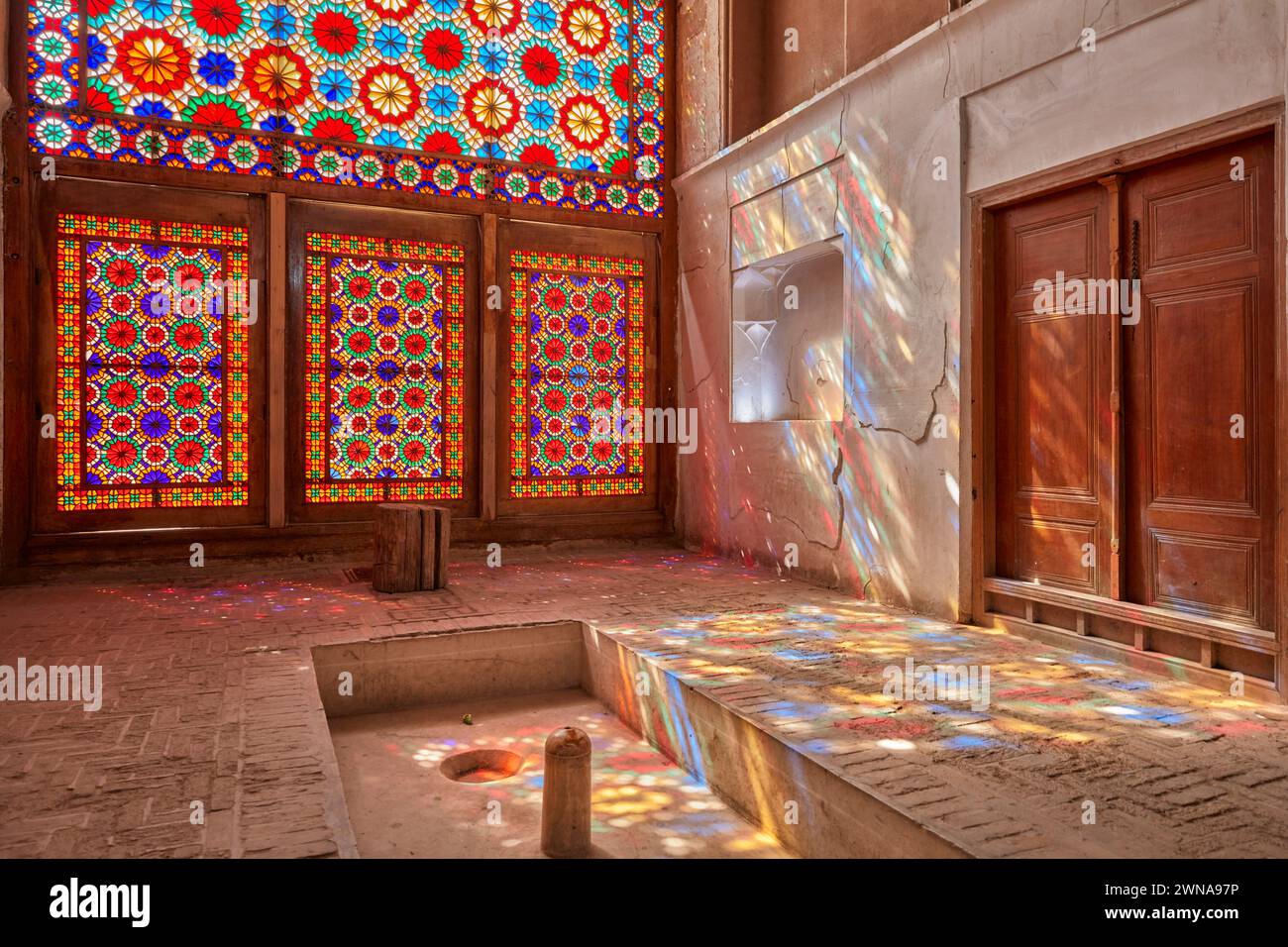 Reich verzierte Buntglasfenster projizieren bunte Lichtspritzer auf Wand und Boden des Pavillons. Dowlatabad Garden, Yazd, Iran. Stockfoto