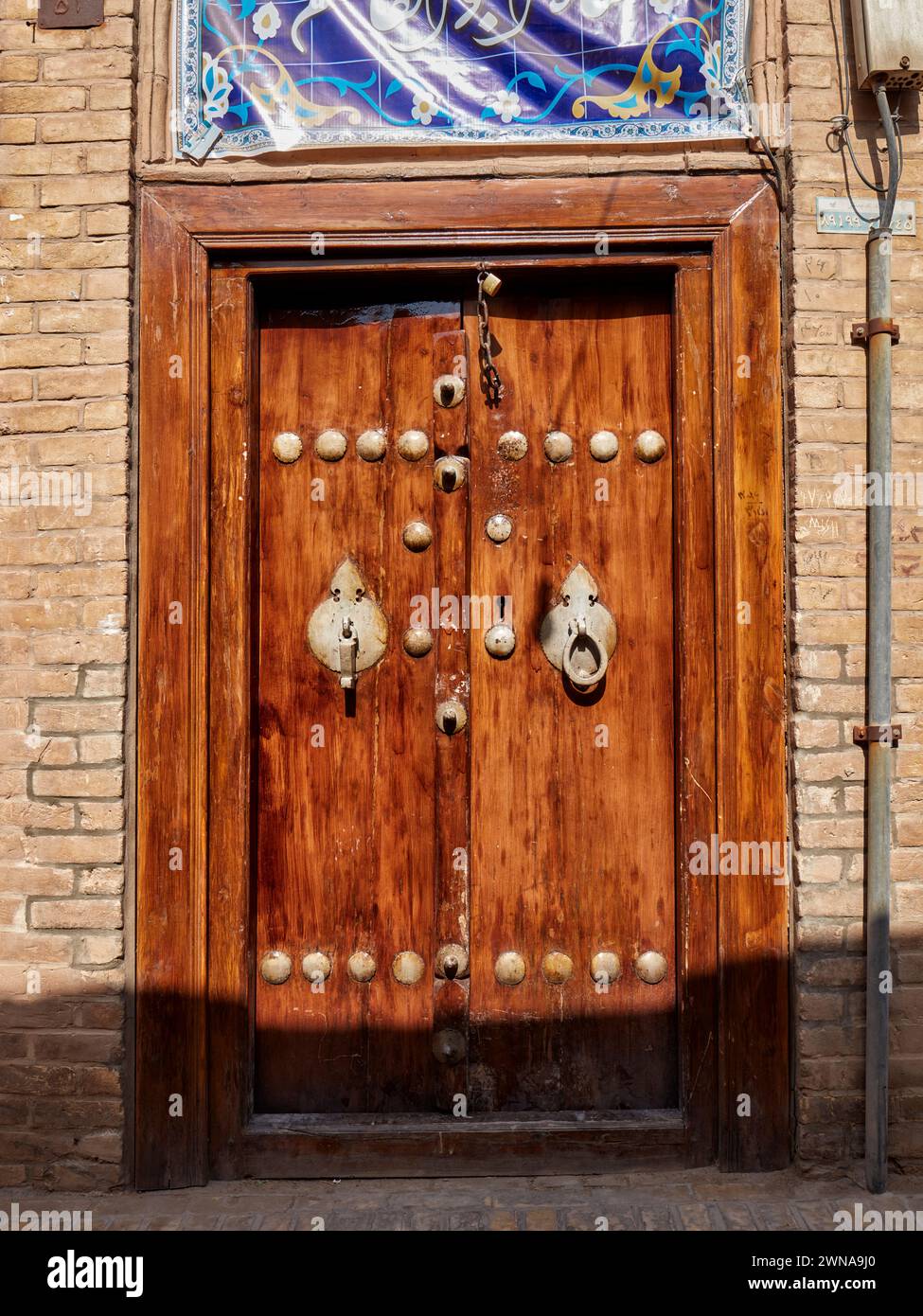 Alte Holztür mit zwei separaten Klopfern - Metallstange für Männer und Metallring für Frauen. Yazd, Iran. Stockfoto
