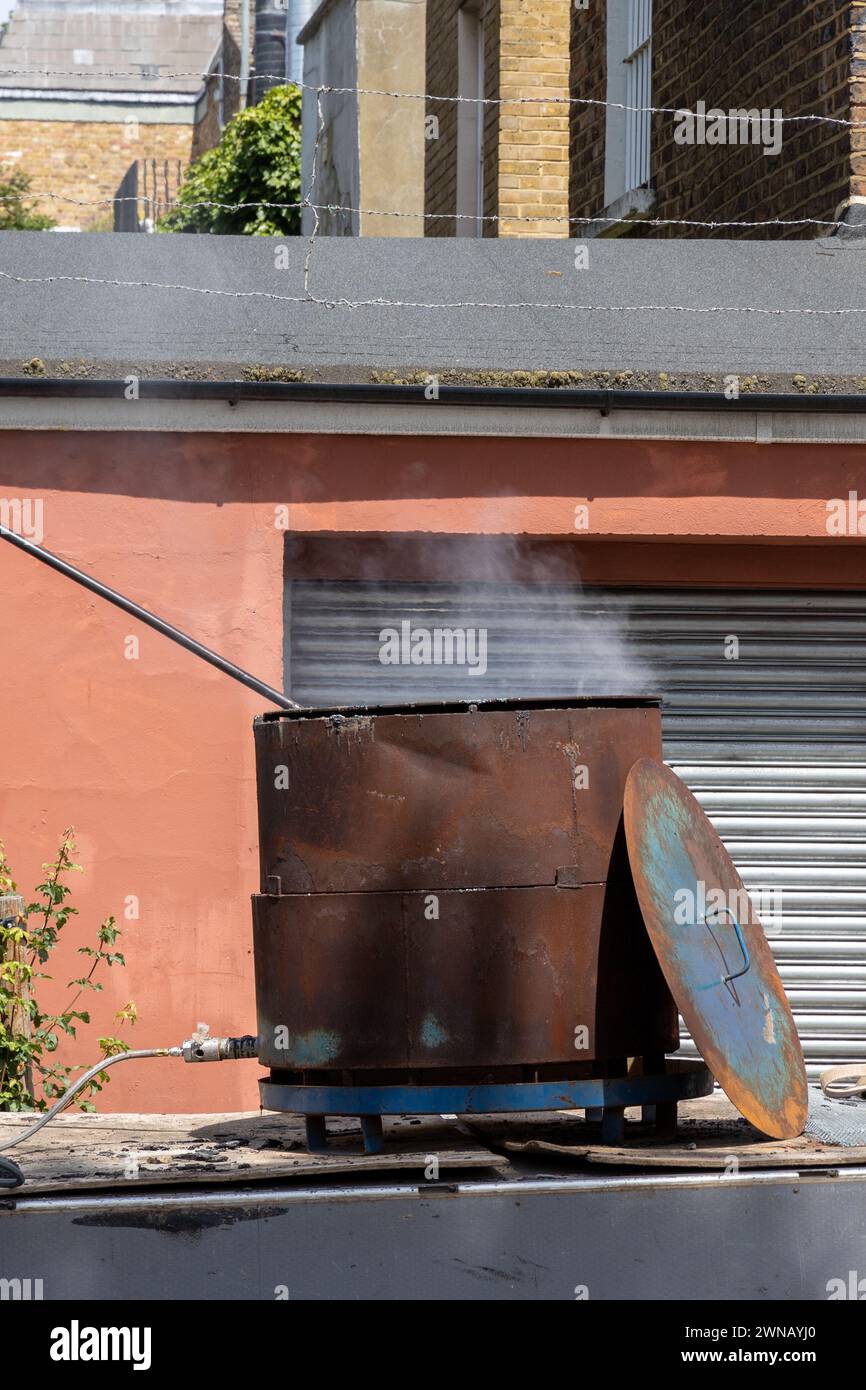 Teer oder Harz kocht auf der Baustelle in rostigem Behälter Stockfoto