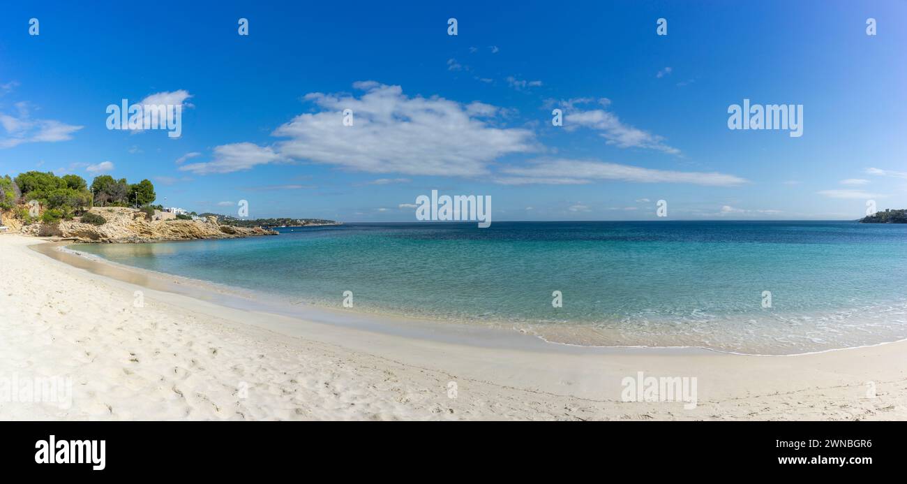 Ein breiter Sandstrand umschließt das türkisfarbene Meer unter einem Wolkenhimmel. Stockfoto