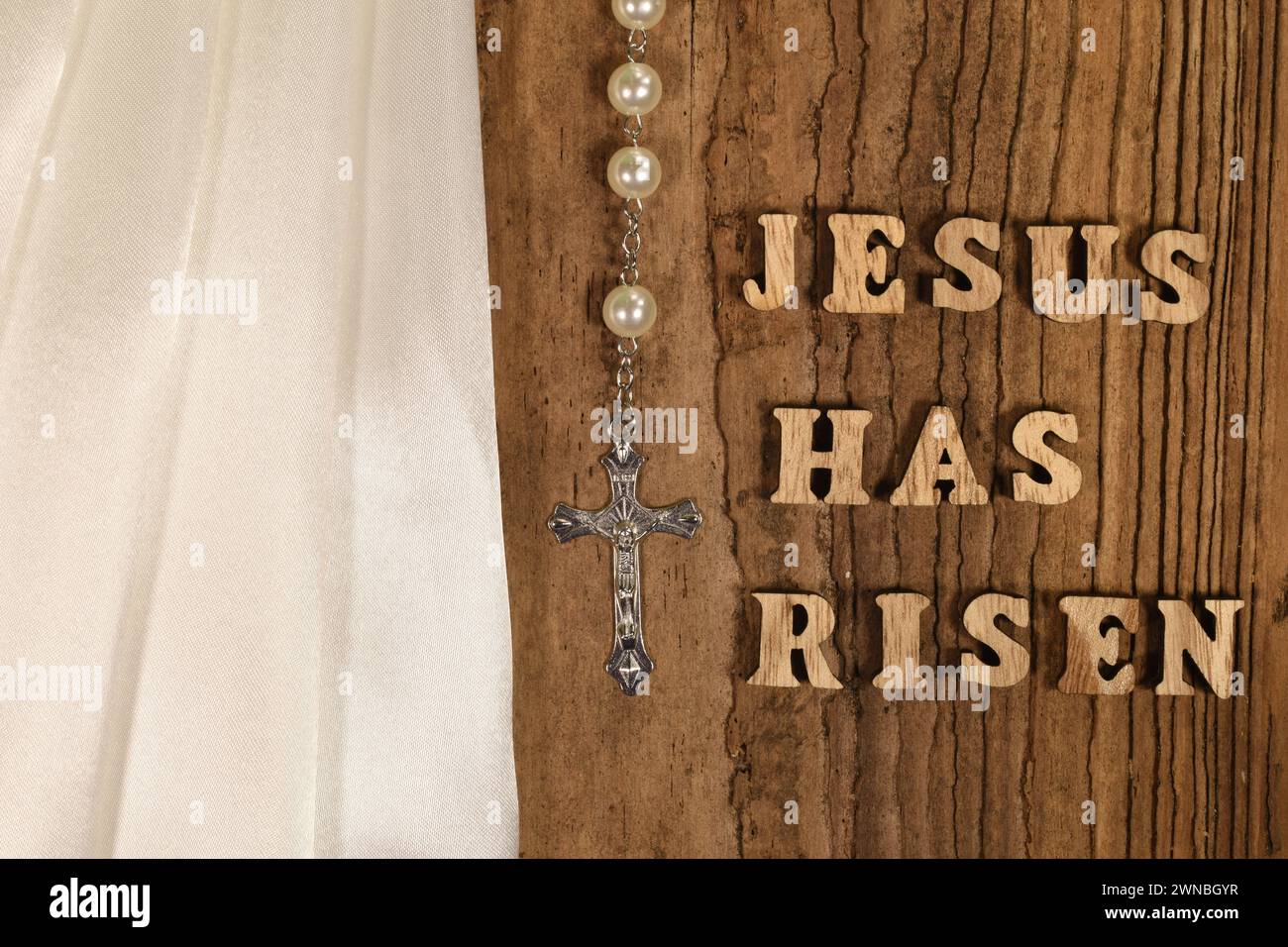 Jesus hat Text auf hölzernem Hintergrund mit Kreuz, Rosenkranz, weißem Tuch und Schneeglöckchen auferstanden Stockfoto