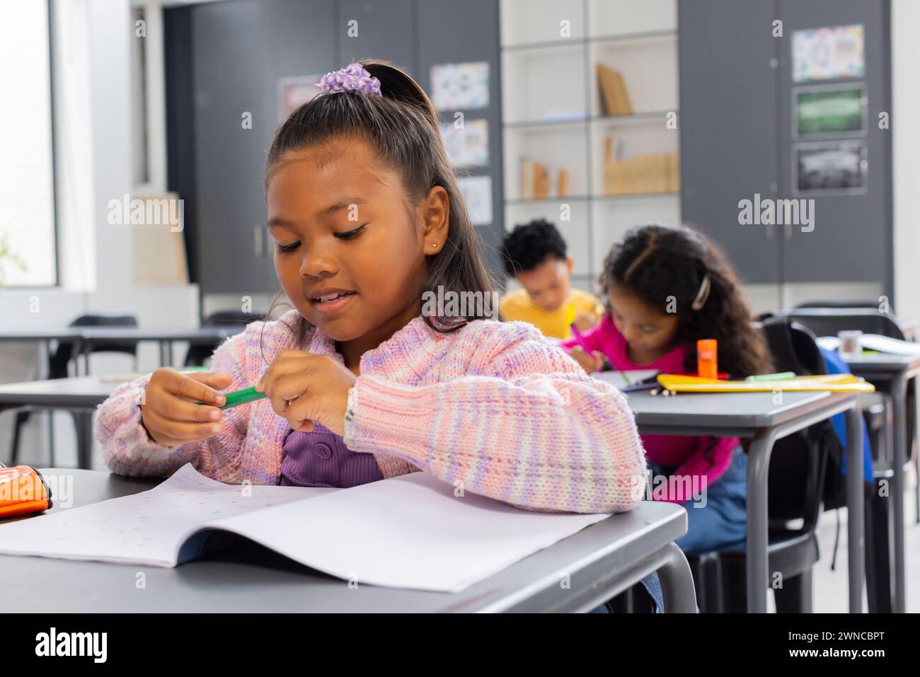 Ein birassisches Mädchen mit lila Haargummis konzentriert sich auf ihre Schularbeit, Bleistift in der Hand Stockfoto