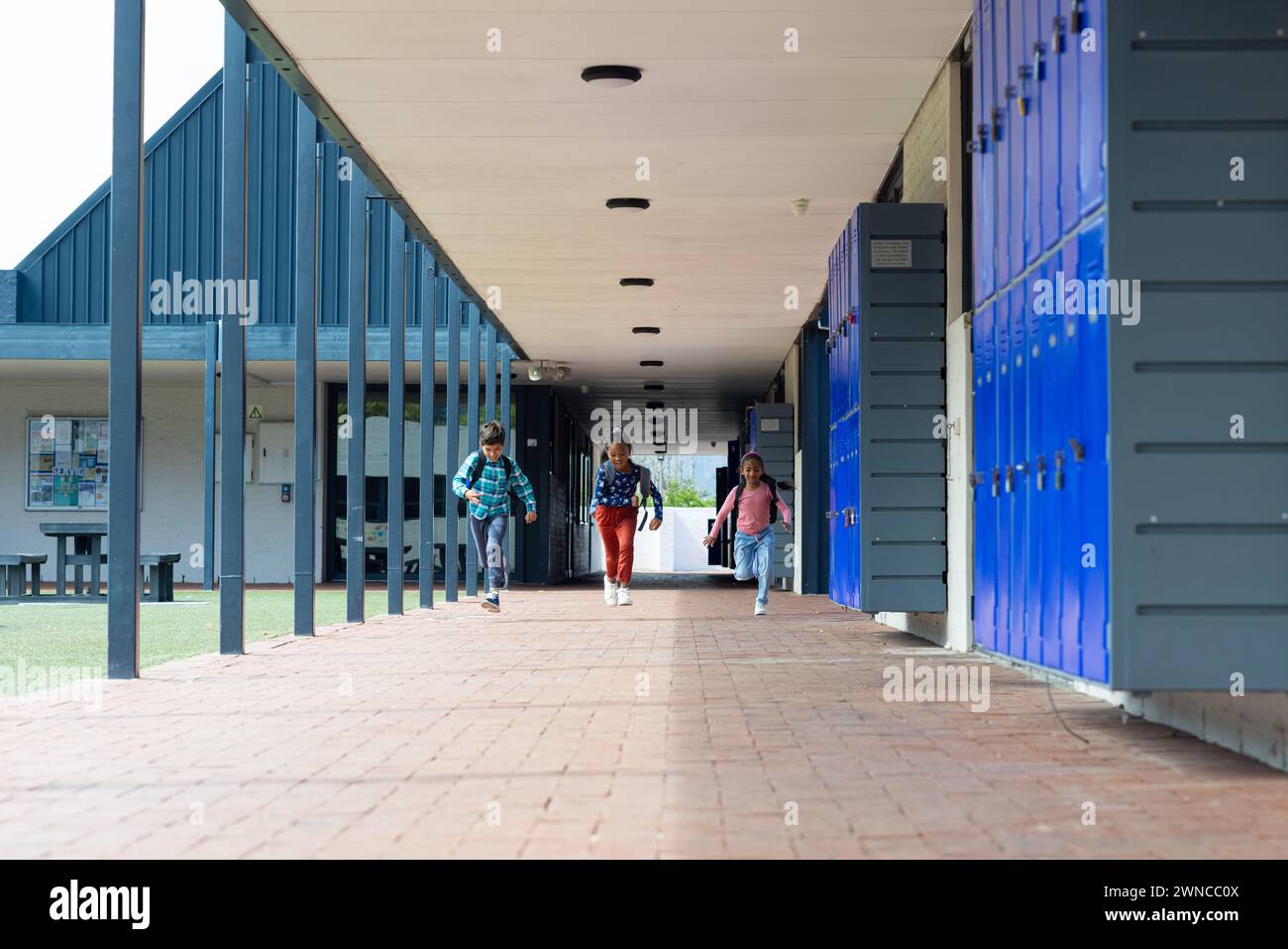Drei Schüler gehen durch einen Schulflur, der mit blauen Schließfächern mit Kopierraum gesäumt ist Stockfoto
