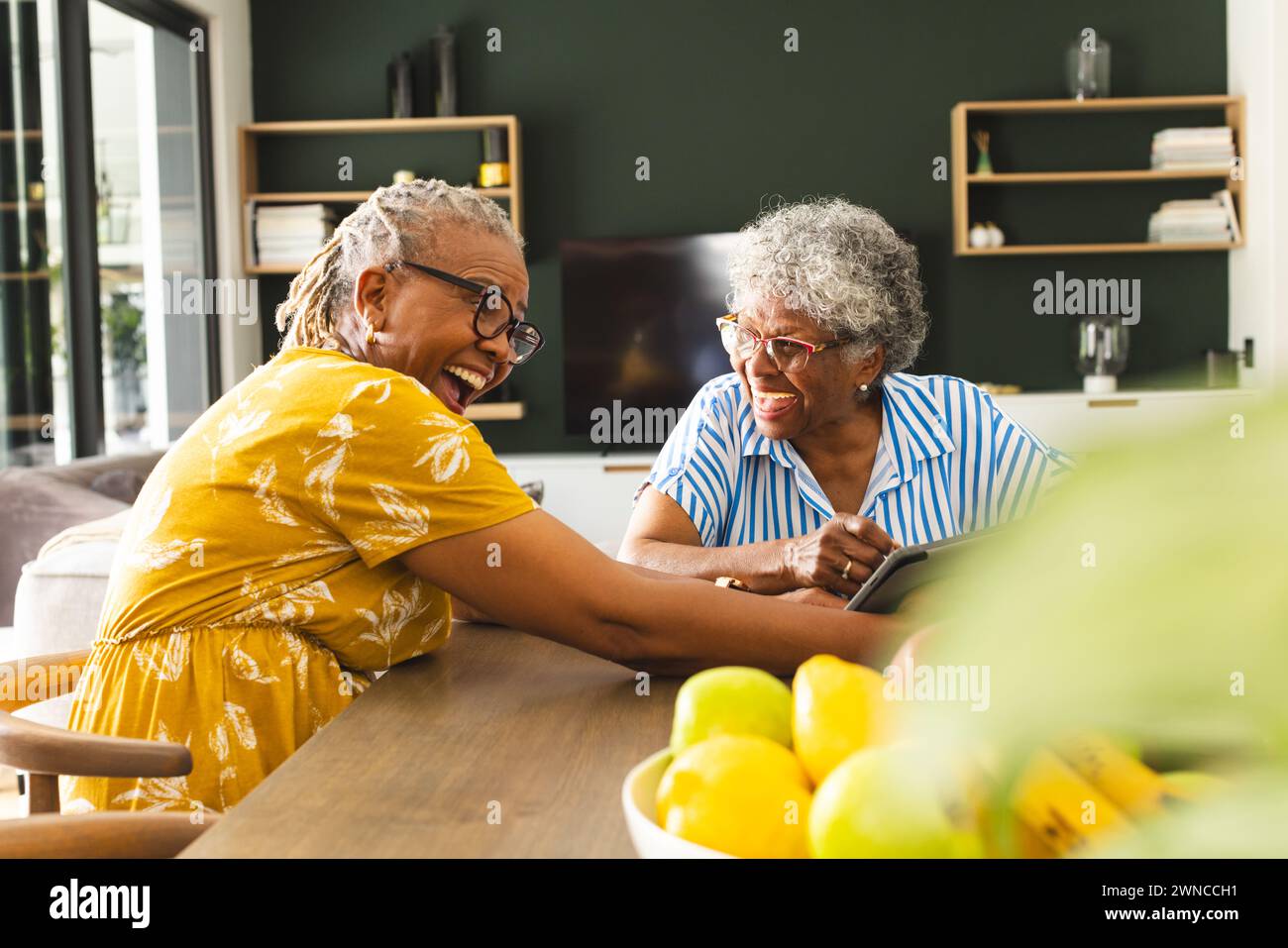 Ältere afroamerikanische Frau und ältere birassische Frau lachen zu Hause über eine Tablette Stockfoto