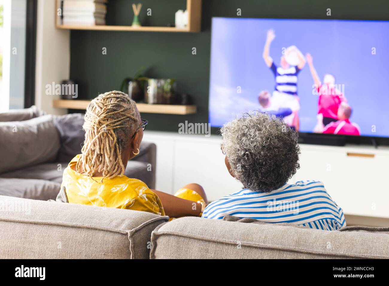 Ältere afroamerikanische Frau und ältere birassische Frau schauen sich Rugby im Fernsehen zu Hause an Stockfoto