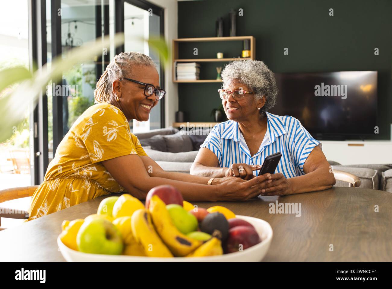 Ältere afroamerikanische Frau und ältere birassische Frau teilen sich einen Moment an einem Tisch zu Hause Stockfoto