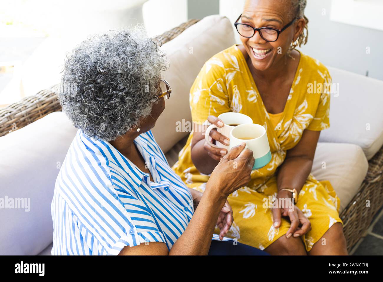 Ältere afroamerikanische Frau und ältere birassische Frau lachen zu Hause über Kaffee Stockfoto