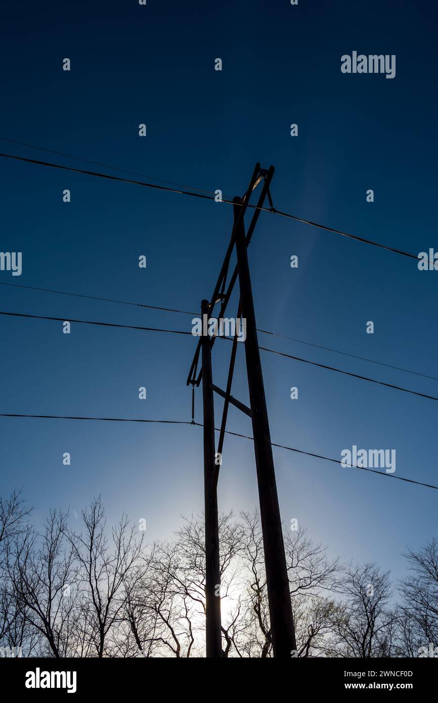 Blauer Himmel und schwache Kondensstreifen silhoutten Strommasten und Übertragungsleitungen. Stockfoto