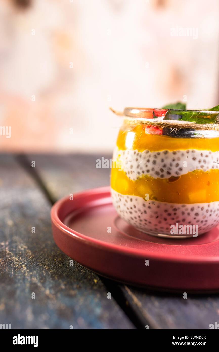 Chia Seed Pudding mit Mango und Beeren im Glasglas auf roter Platte Stockfoto