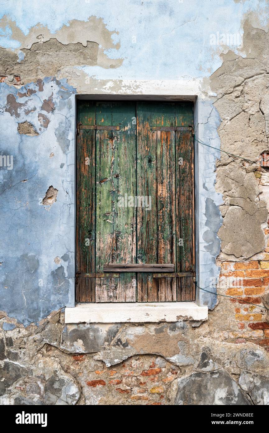 Ein altes hölzernes Fensterfenster in einer freiliegenden Gipswand in Venedig Italien. Stockfoto