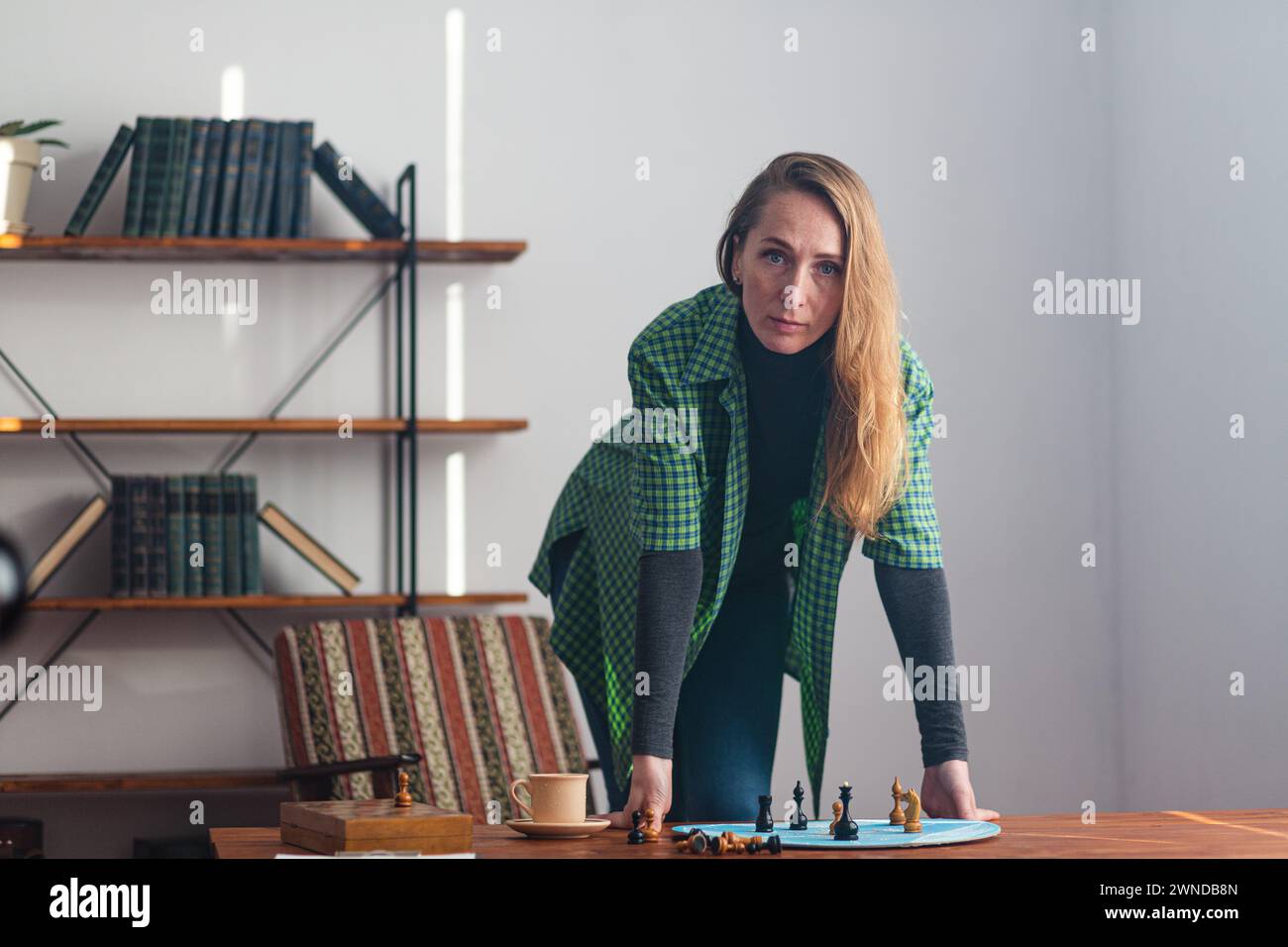 Porträt einer zielgerichteten Frau steht mit den Händen auf dem Tisch und blickt aufmerksam vor ihr. Auf dem Tisch befinden sich Schachfiguren auf einem blauen ci Stockfoto