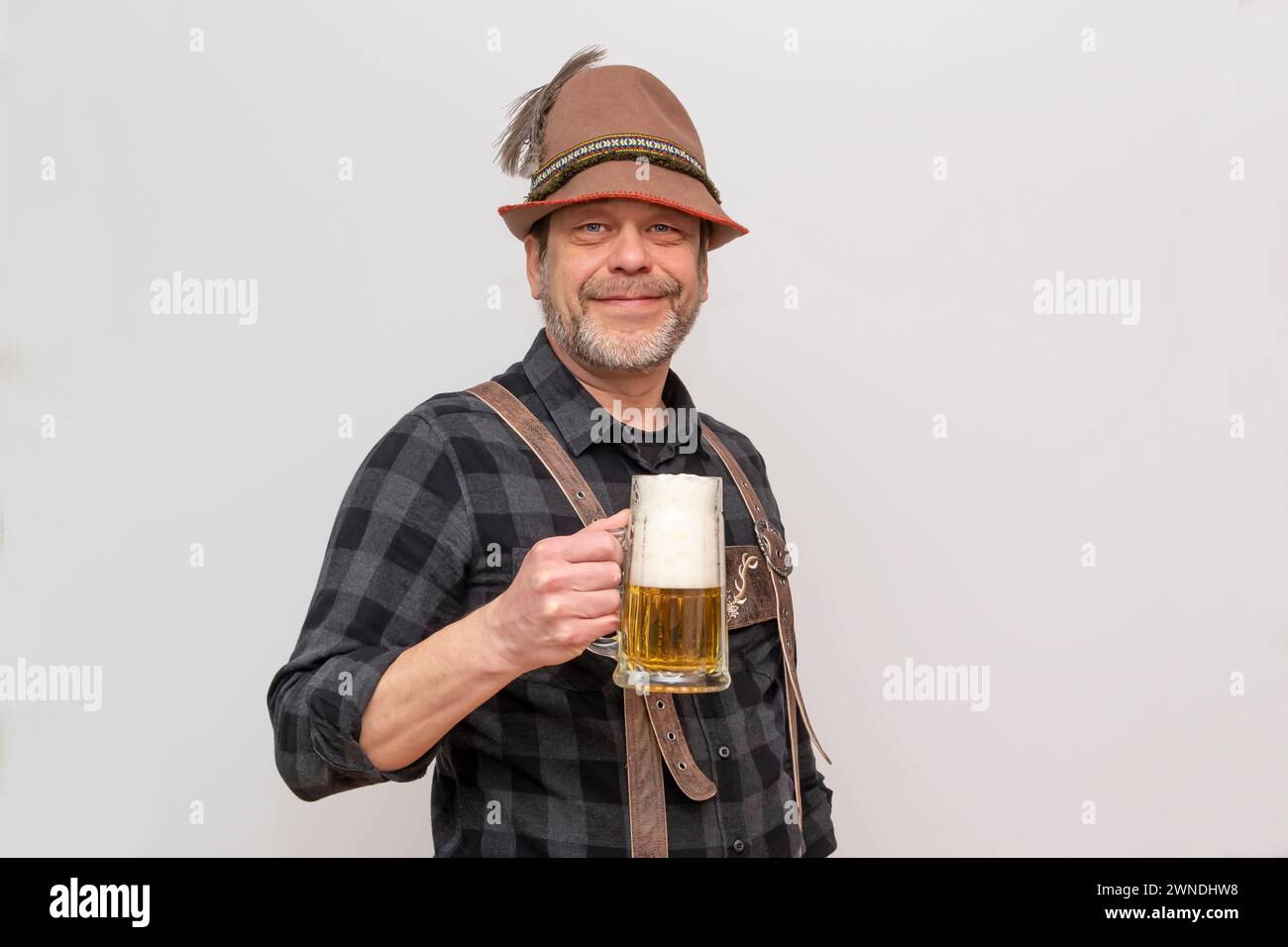 Älterer bärtiger Mann mit Hut will ein Glas Bier mit Schaum trinken, Bierfest in Österreich und Deutschland. Stockfoto