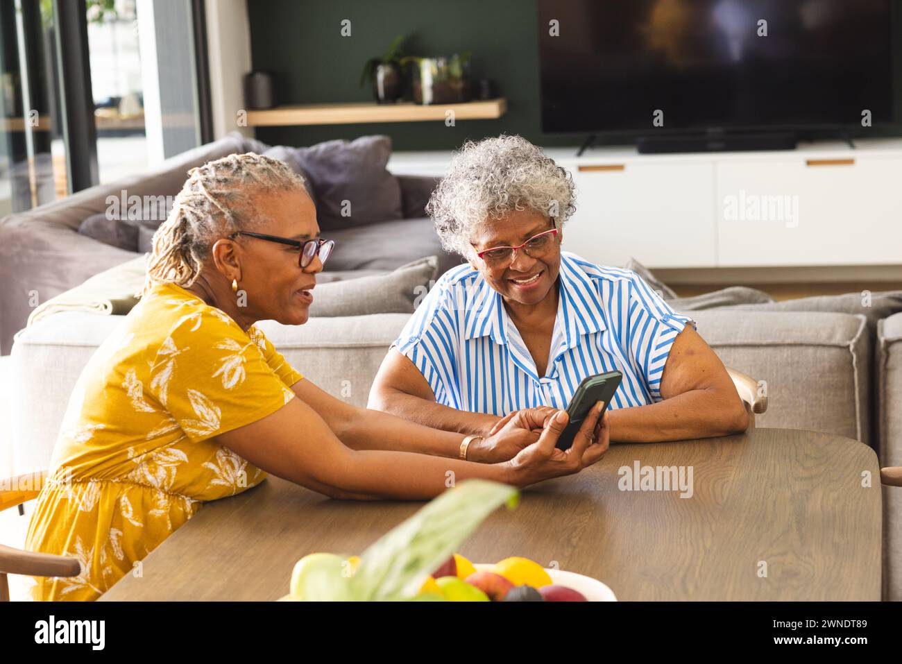 Ältere afroamerikanische Frauen und Frauen mit birassischer Herkunft sehen sich zu Hause ein Smartphone an Stockfoto
