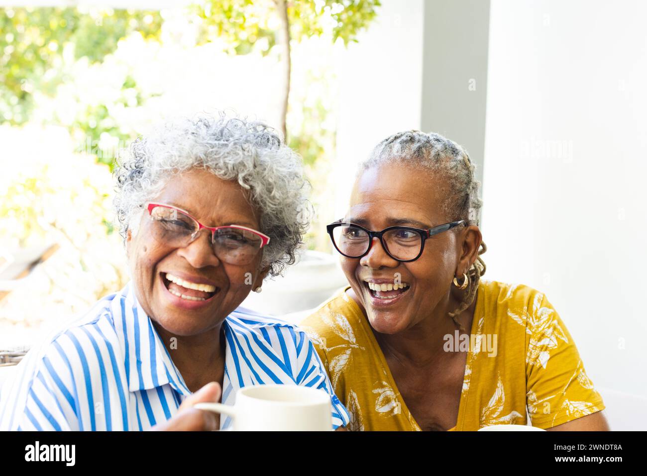 Hochrangige afroamerikanische Frau und birassische Frau teilen sich einen freudigen Moment und lachen zu Hause zusammen Stockfoto