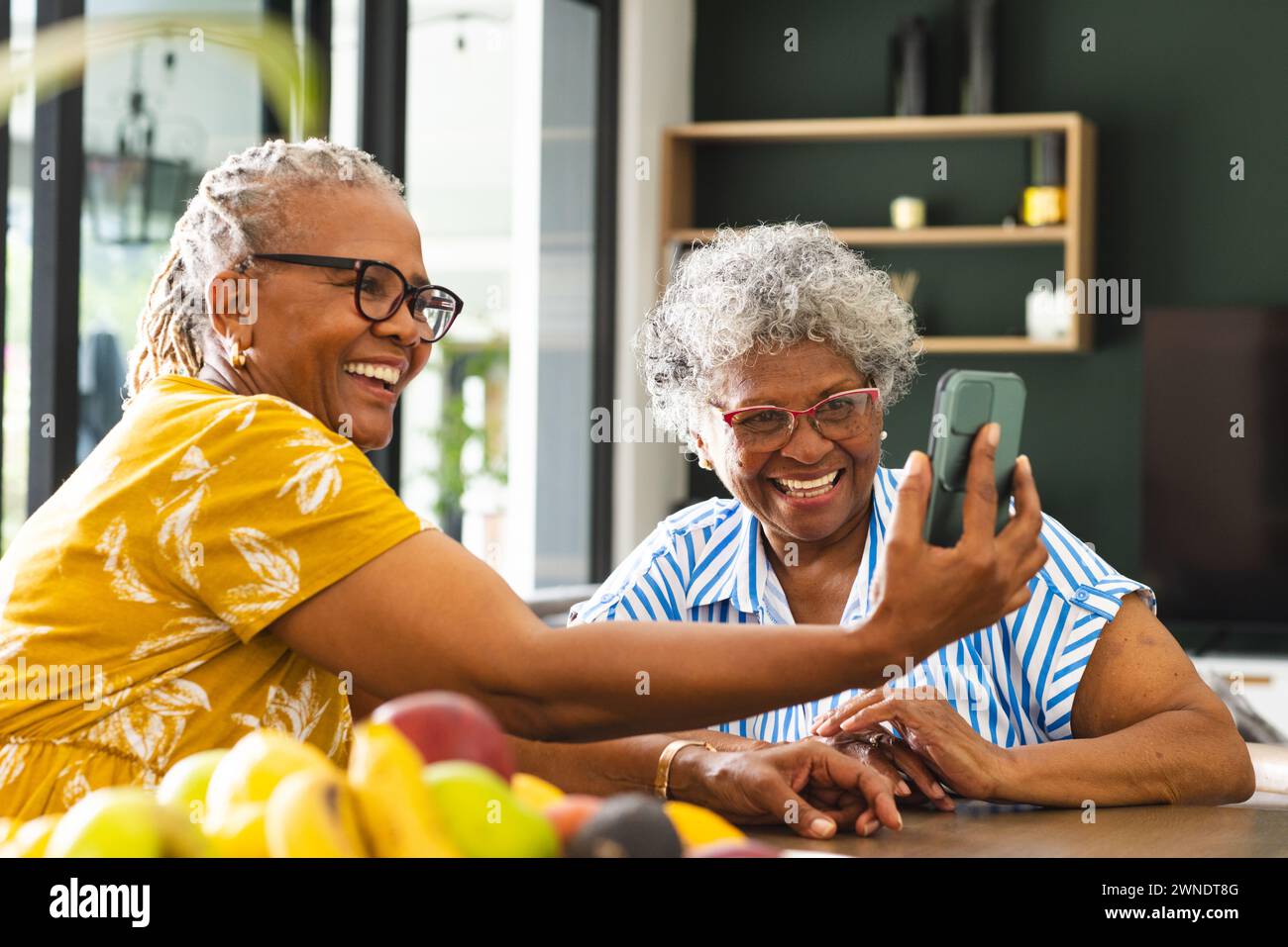 Ältere afroamerikanische Frauen und Frauen mit birassischer Herkunft teilen einen freudigen Moment über ein Smartphone zu Hause Stockfoto