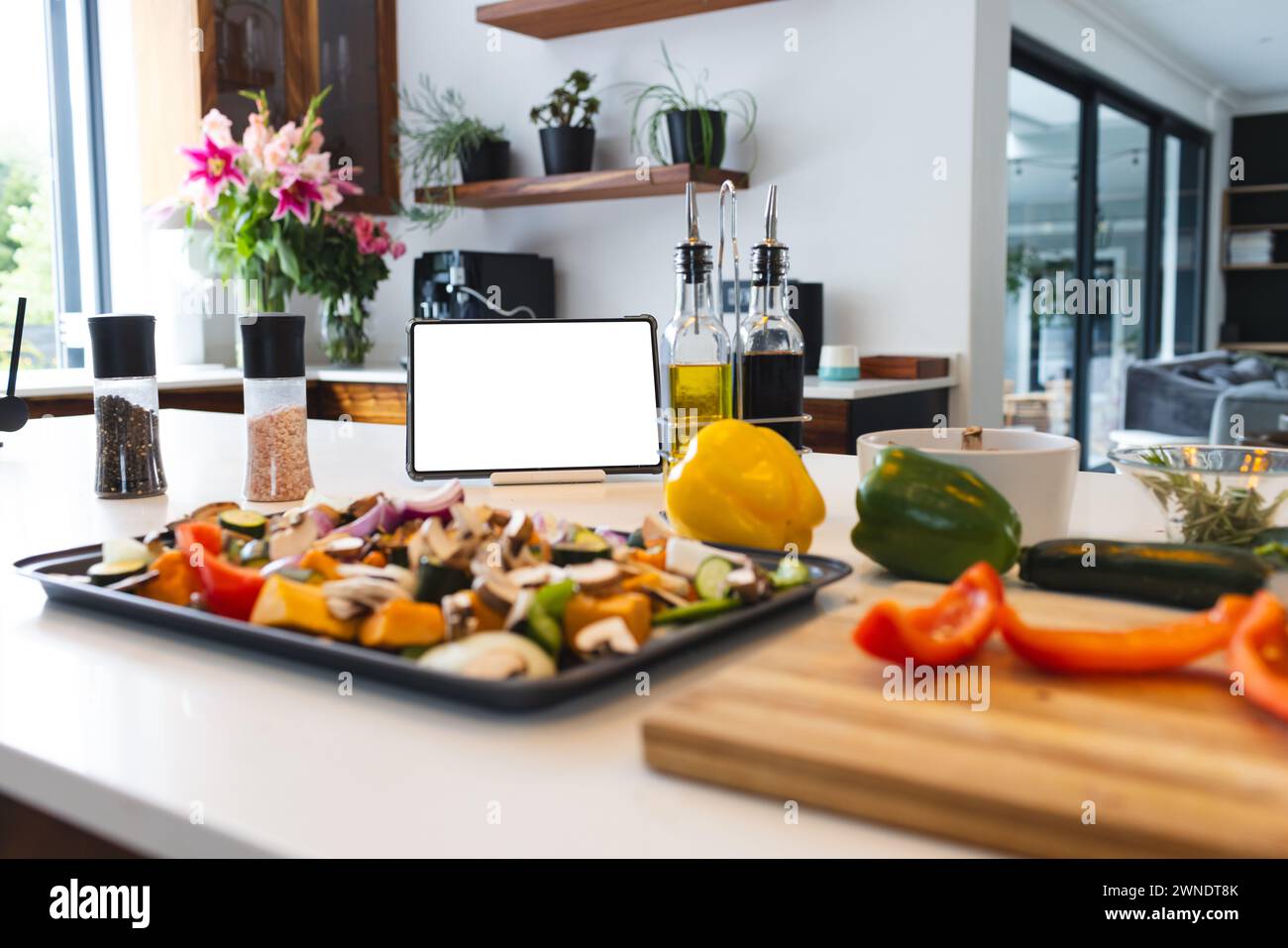 Ein Tablet mit einem leeren Bildschirm steht neben verschiedenen Kochzutaten auf einer Küchenzeile Stockfoto