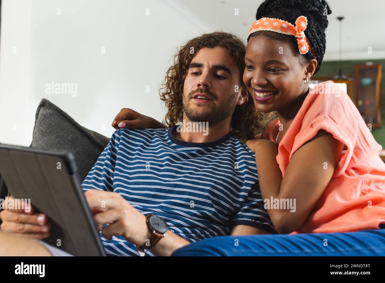 Verschiedene Paare, junger kaukasischer Mann und Afroamerikanerin teilen sich eine Tafel, gemütlich auf einer Couch Stockfoto