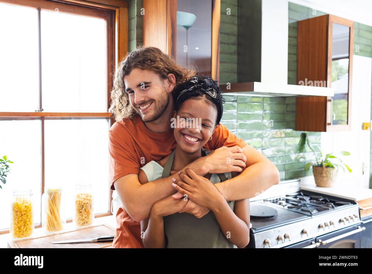 Verschiedene Paare junger Kaukasier umarmt eine junge afroamerikanische Frau in einer sonnigen Küche Stockfoto