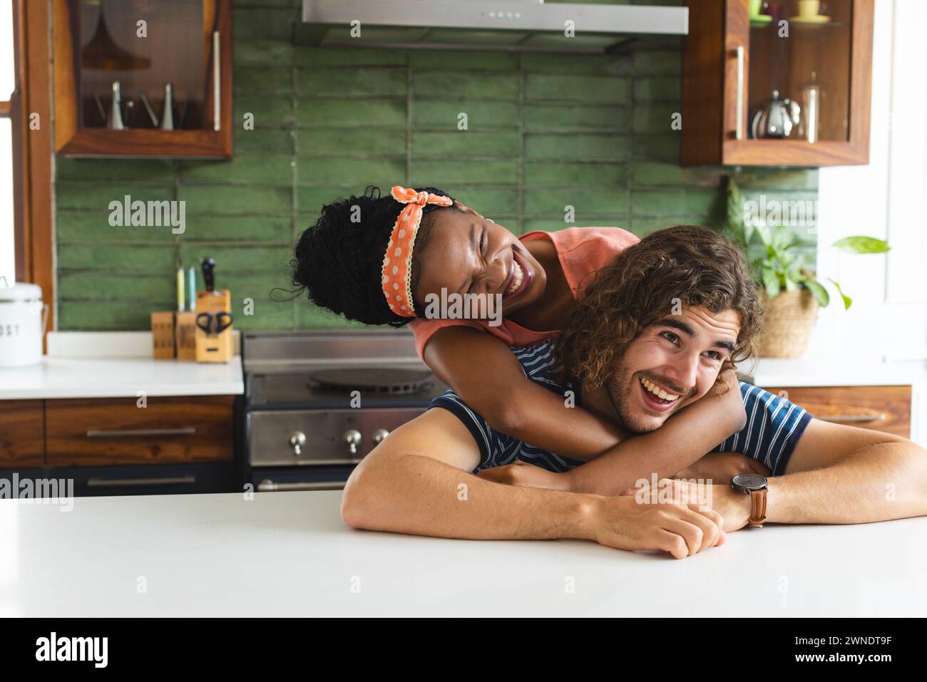 Verschiedene Paare junge afroamerikanische Frau umarmt einen jungen kaukasischen Mann von hinten in einer Küche Stockfoto