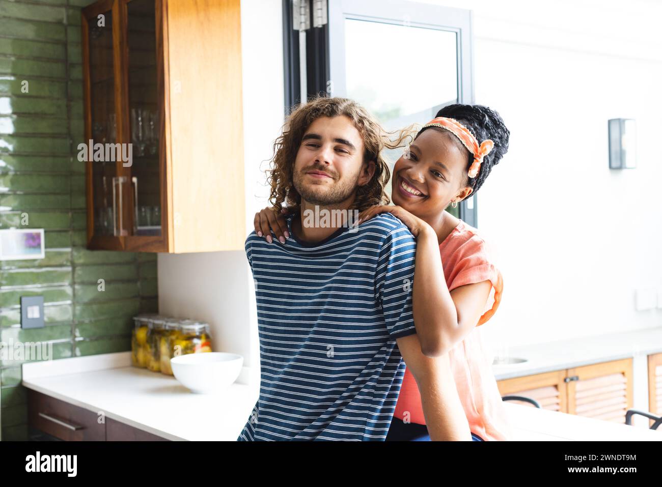 Diverse Paare junge afroamerikanische Frau umarmt einen jungen kaukasischen Mann in einer gemütlichen Küche Stockfoto