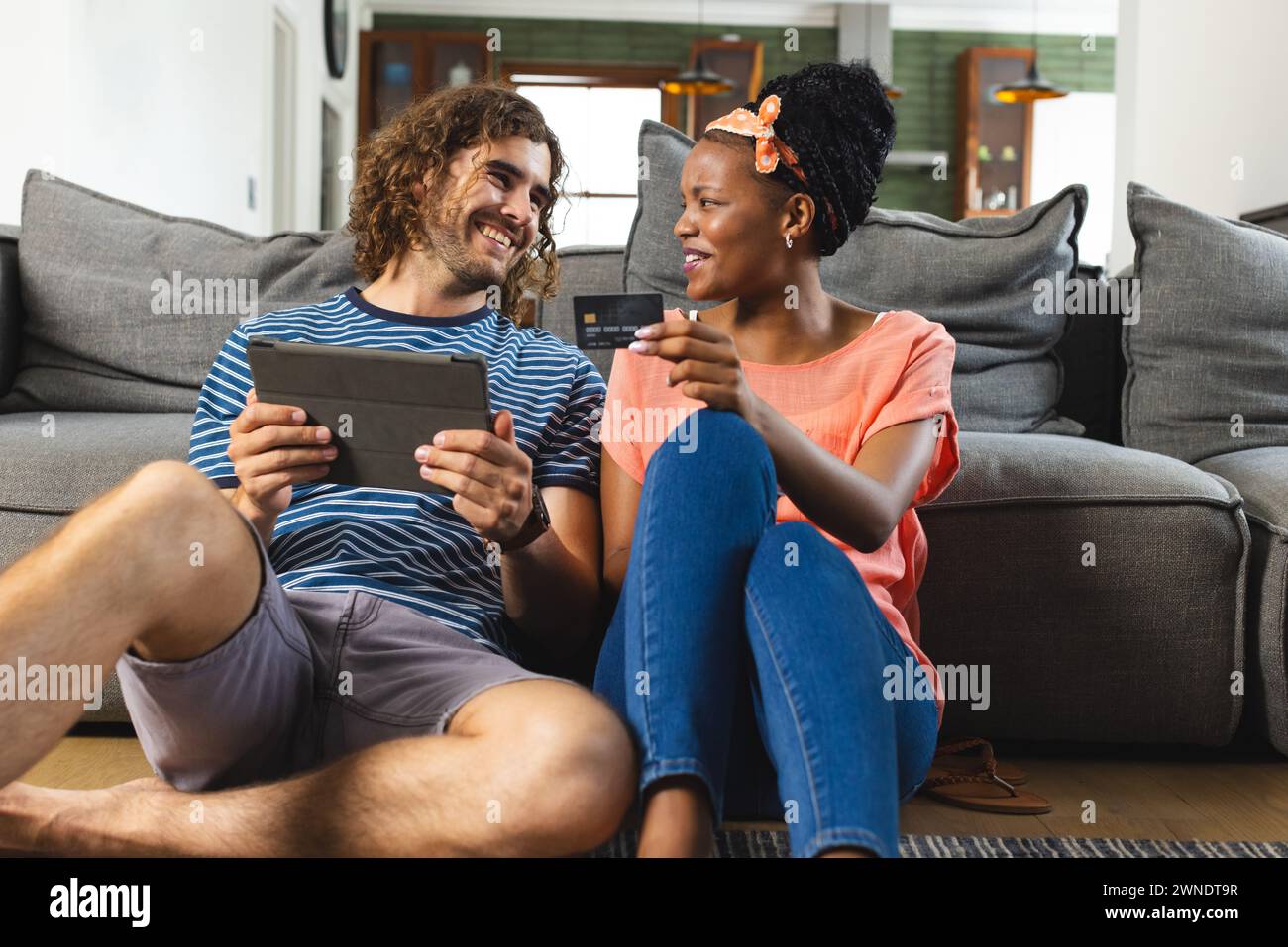 Verschiedene Paare, junger Kaukasier und Afroamerikanerin teilen sich eine Tablette, die auf einer grauen Couch sitzt Stockfoto