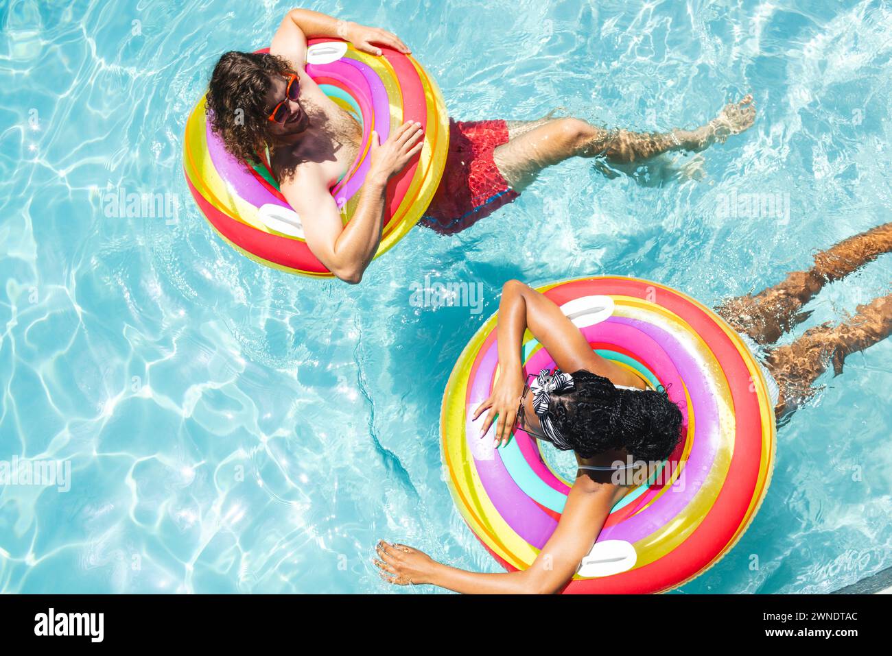 Ein vielseitiges Paar, ein junger Kaukasier und eine Afroamerikanerin entspannen sich auf farbenfrohen Schwimmbecken Stockfoto