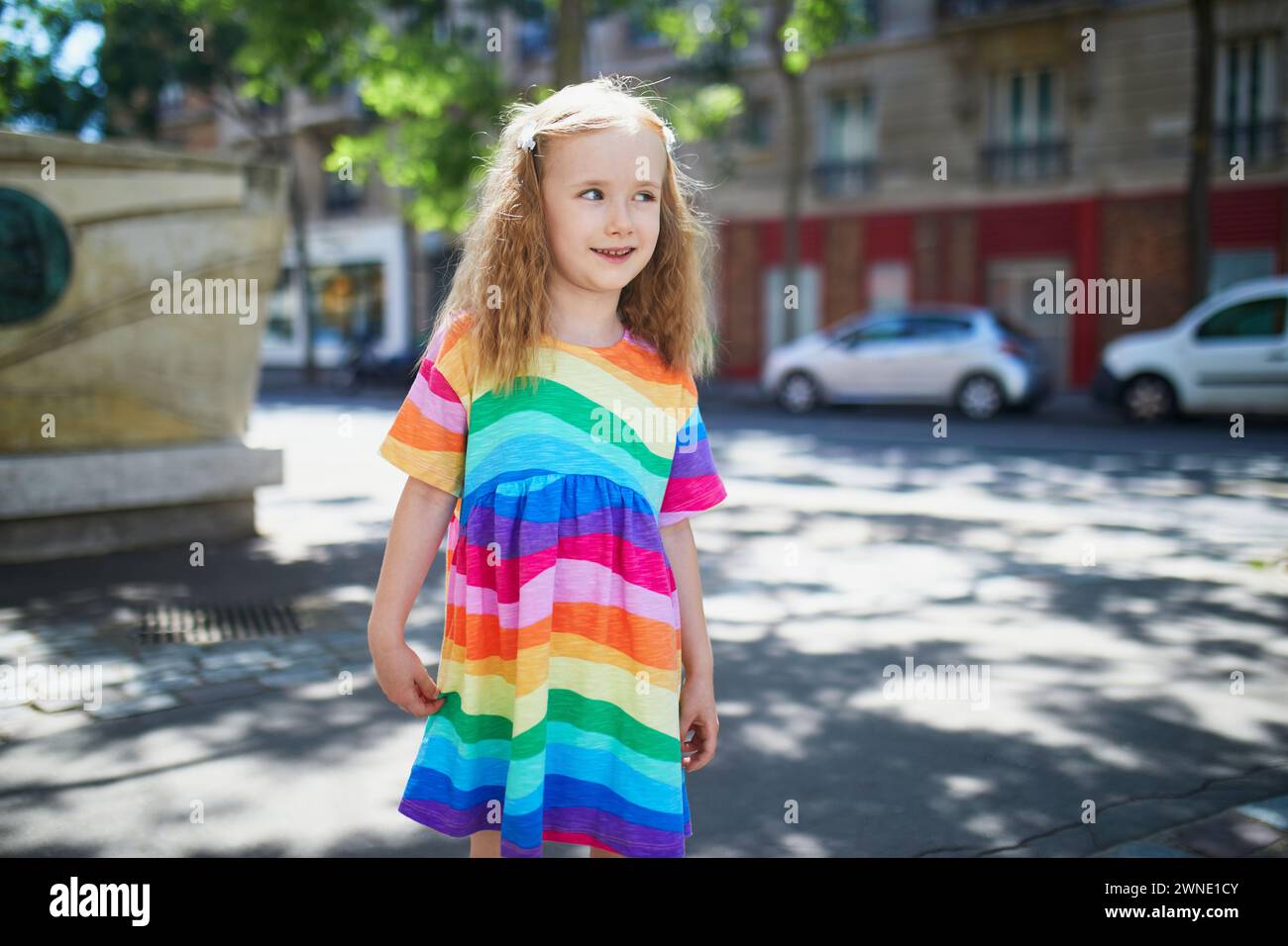 Niedliches Mädchen im Vorschulalter im Regenbogenkleid auf einer Straße von Paris an einem Sommertag Stockfoto