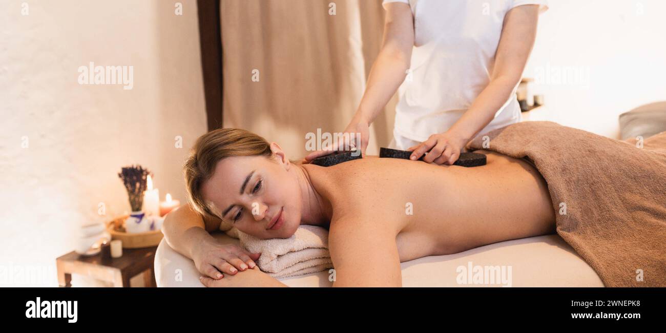 Hot-Stone-Behandlung im Wellness-Spa-Resort. Niedliche Frau während der Hot Stone Massage, Seitenansicht Stockfoto