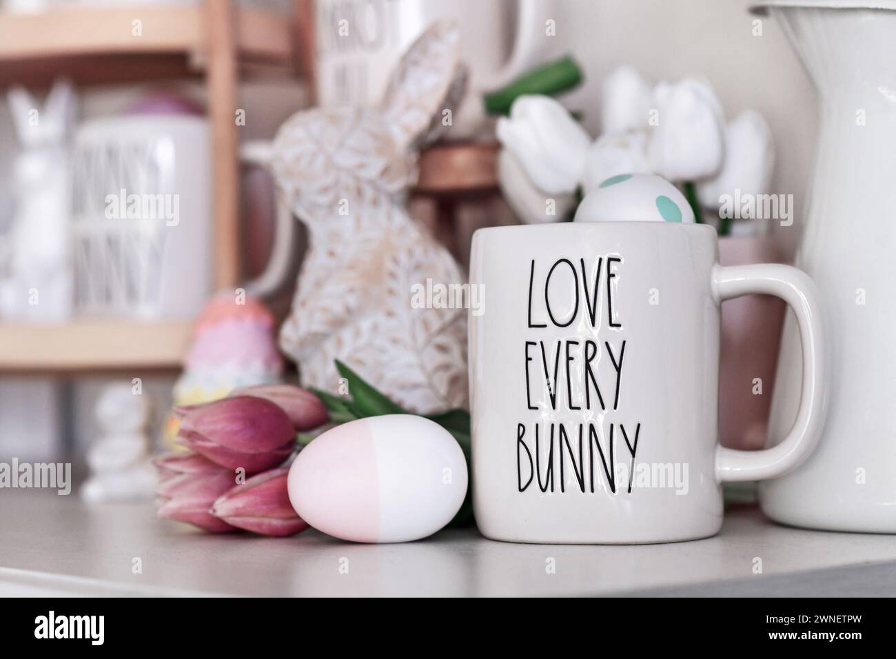 Deutschland - März 2024: Saisonale Osterhausdekoration mit Rae Dunn Becher mit Text 'Love Every Bunny', Osterei, Tulpenfrühlingsblumen Stockfoto