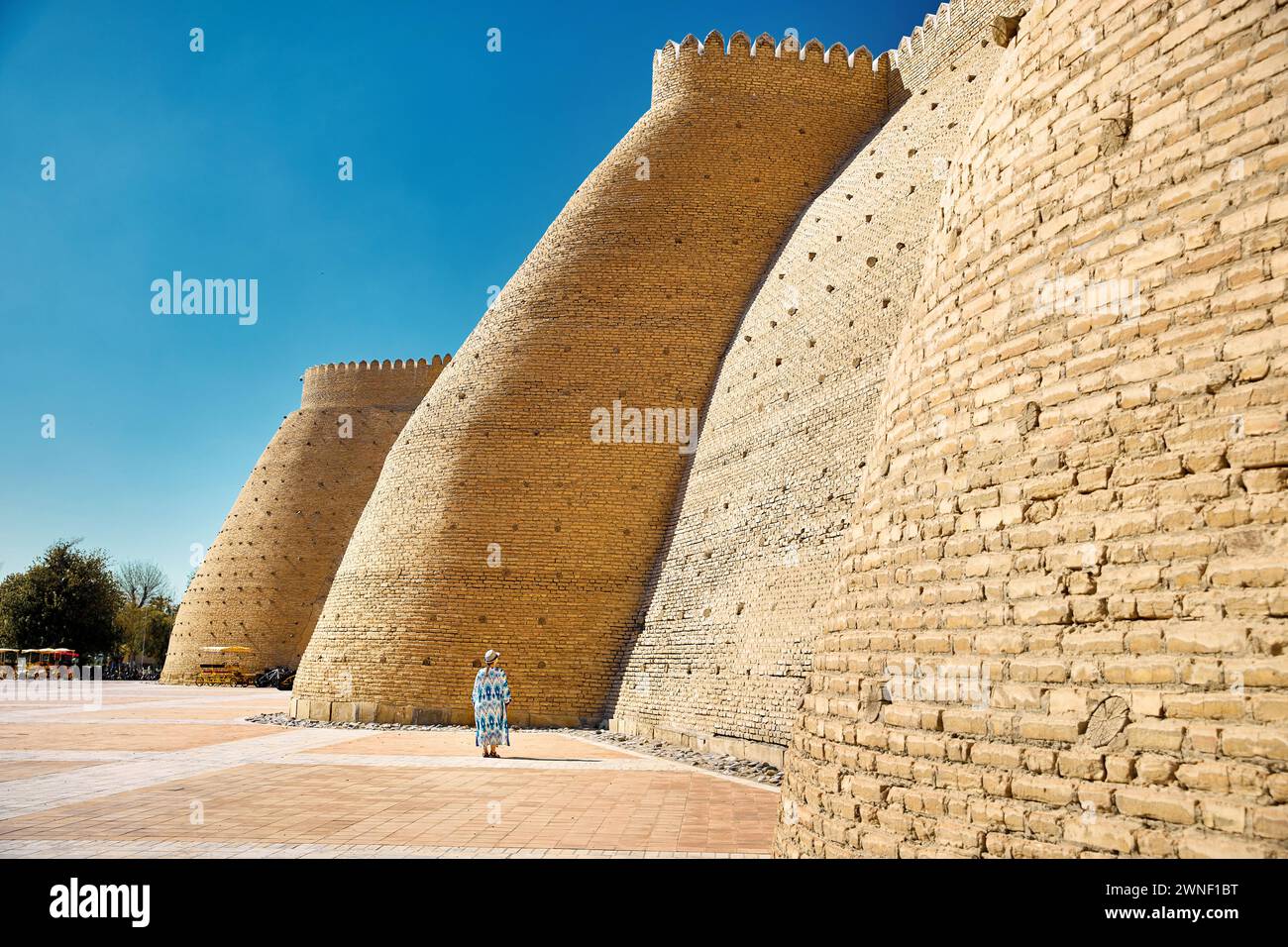 Frau in ethnischer Kleidung mit blauem traditionellem Muster in der Nähe der Mauern der Arche Buchara in Usbekistan. Stockfoto