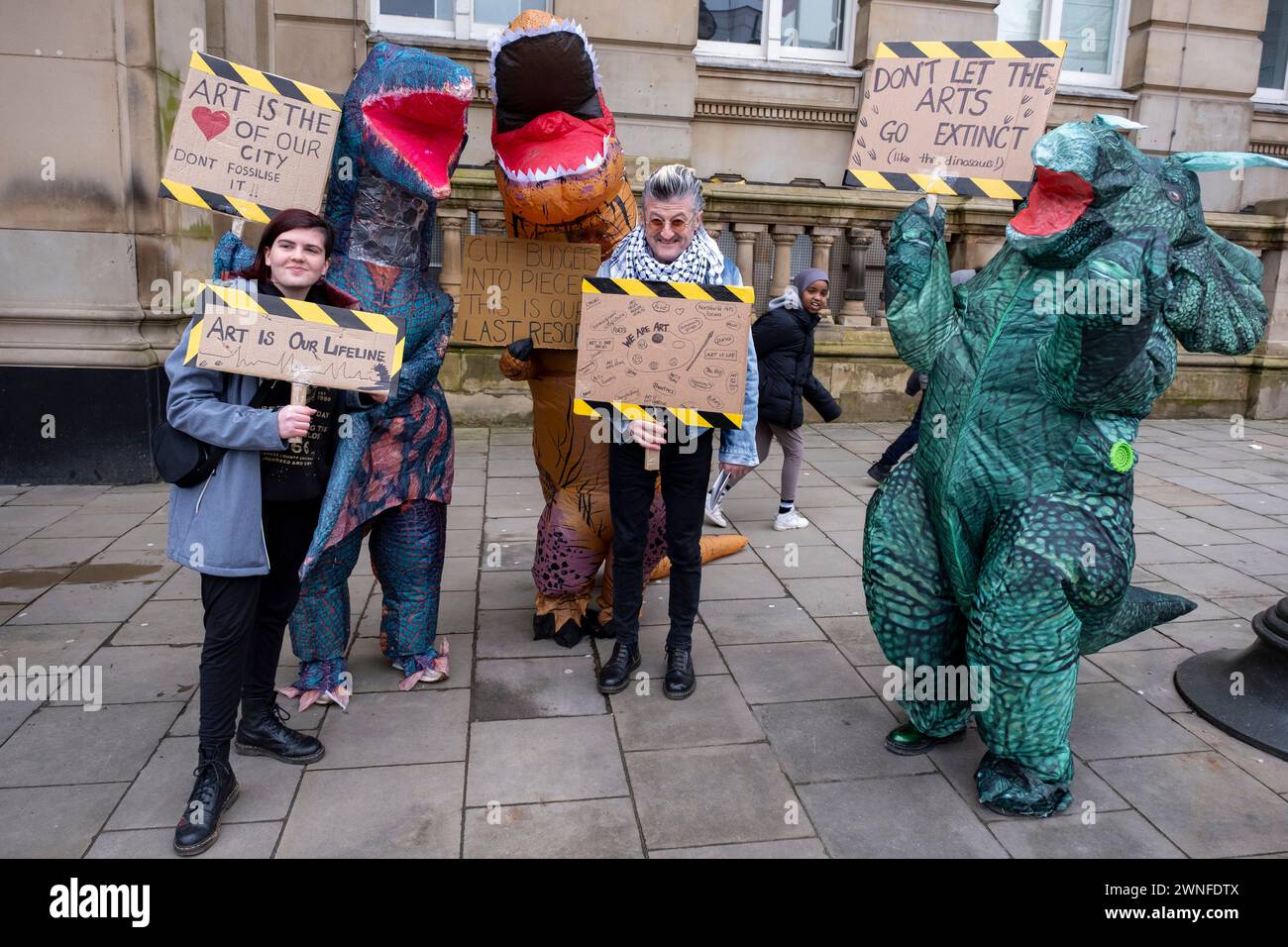 Demonstranten verkleideten sich als Dinosaurier gegen Schnitte in den Künsten mit dem lokalen Dichter Spoz bei der Demonstration Stand Up for Public Services gegen Kürzungen des Stadtrates von Birmingham am 2. März 2024 in Birmingham, Großbritannien. Der Protest ruft Einwohner, Arbeiter und Gewerkschaften in der ganzen Stadt auf, sich gegen verheerende Kürzungen des rates zu versammeln, die derzeit etwa 376 Millionen Pfund für Dienstleistungen betragen, die wahrscheinlich große Auswirkungen auf die Bewohner haben werden. Zu den Bereichen, in denen Kürzungen vorgenommen werden sollen, gehören Jugenddienste, Verkehr, Müllsammlungen, Bibliotheken und Kunstorganisationen. Der von der Labour-Partei betriebene rat ha Stockfoto