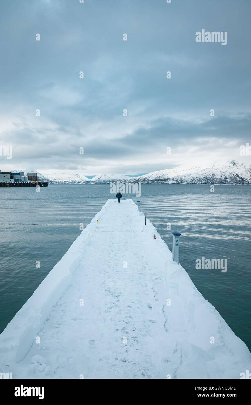 Entfernte Person auf einem langen, schneebedeckten Pier in einem norwegischen Fjord Stockfoto