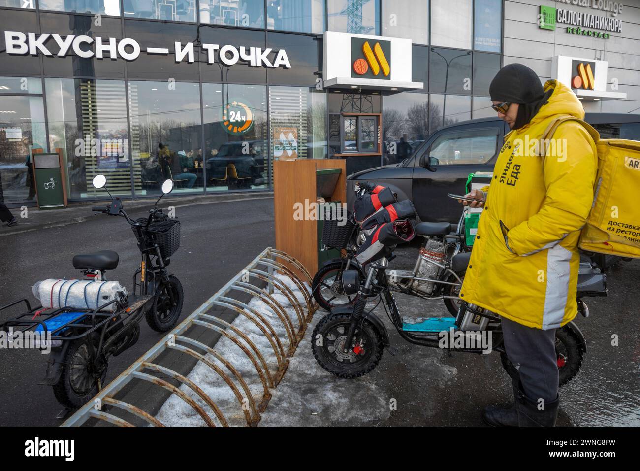 Moskau, Russland. März 2024. Ein Kurier des Yandex Go Food Delivery Service akzeptiert eine Bestellung an einem Eingang zu 'Vkusno - and Tochka' (eng:'Delicious. Und Full Stop') Fast-Food-Restaurant in einem Wohngebiet von Moskau, Russland Stockfoto