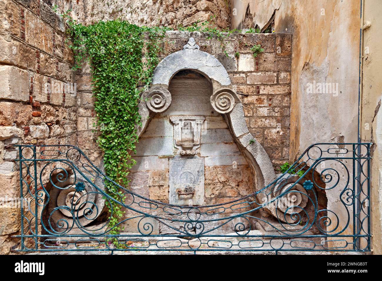 Alter ottomanischer Brunnen aus dem späten 18. Jahrhundert, mit religiösen Schriften in ottomanischem Alphabet und geschützt durch Metallgeländer, in der Altstadt von Nafplio. Stockfoto